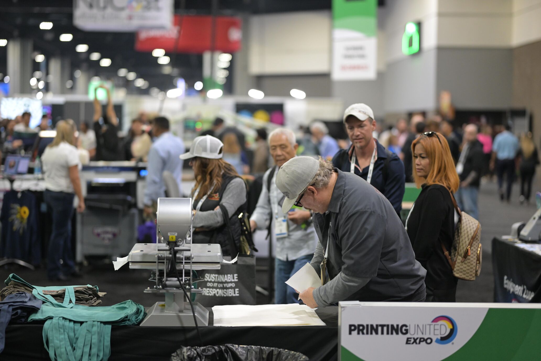 Man operating a direct-to-garment machine while attendees watch at PRINTING United Expo