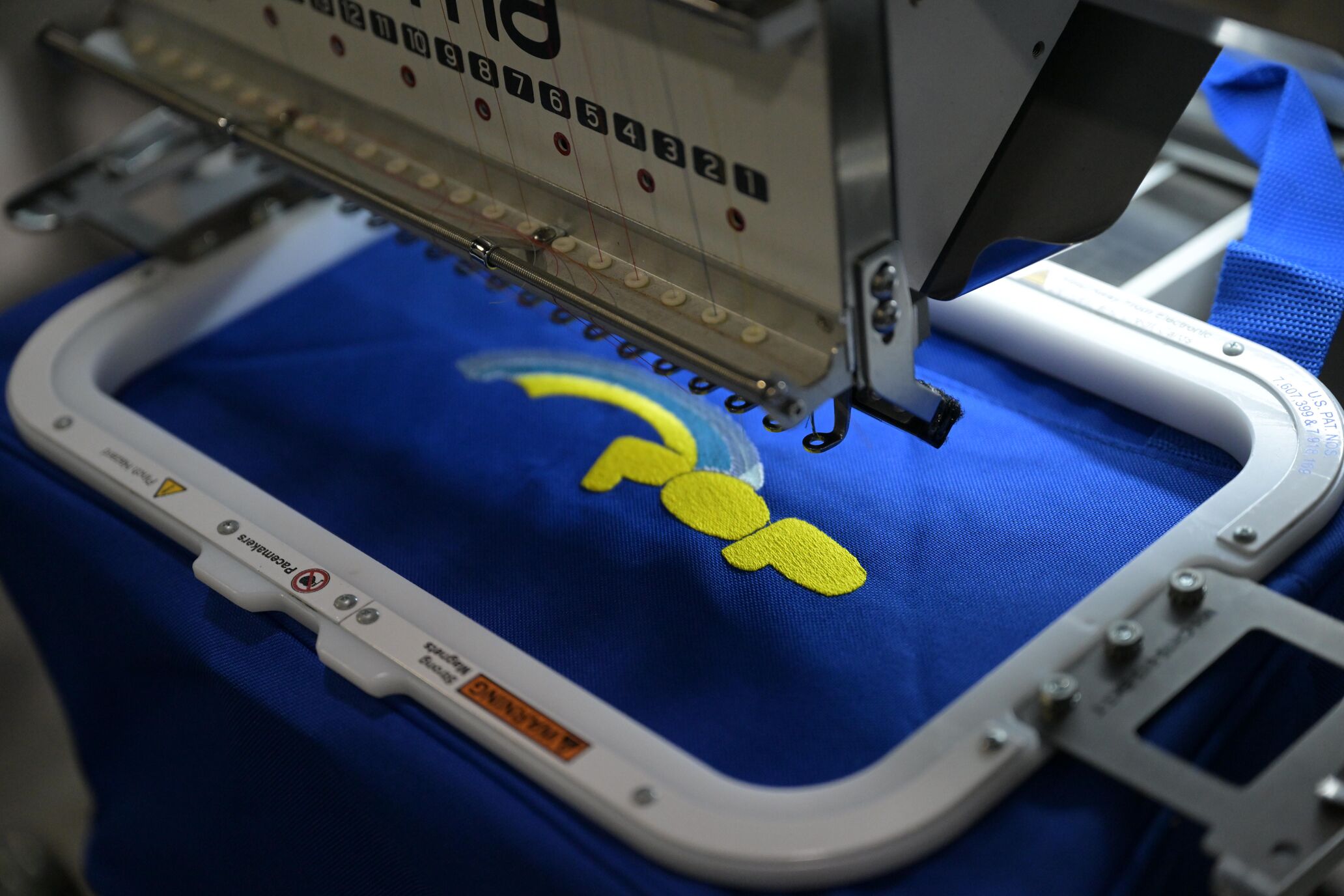 Close-up photo of an embroidery machine embroidering yello text on blue fabric
