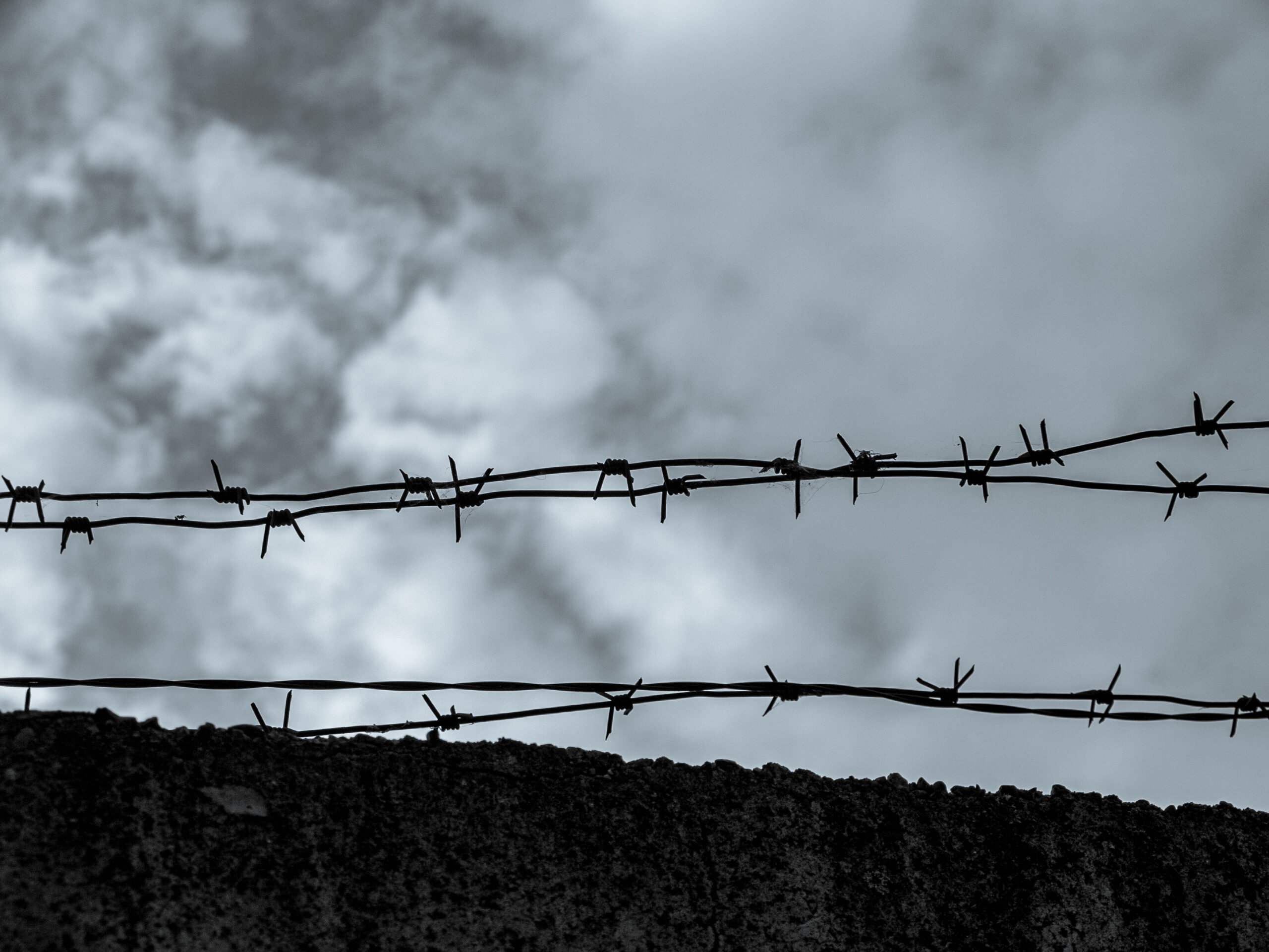 Black and white image of a barbed wire fence with a cloudy sky in the background