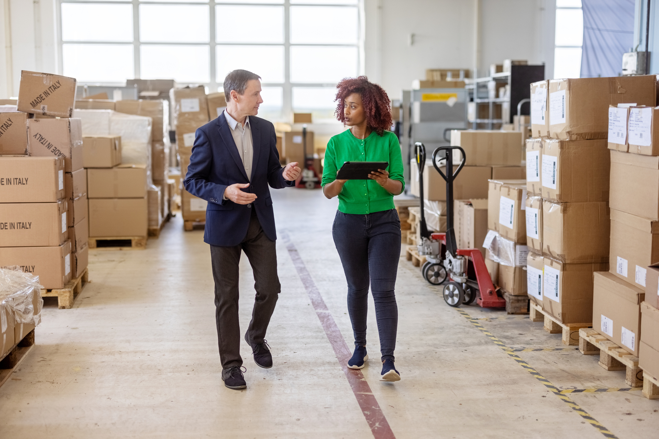 Man and woman walking through a shipping area with boxes stacked up