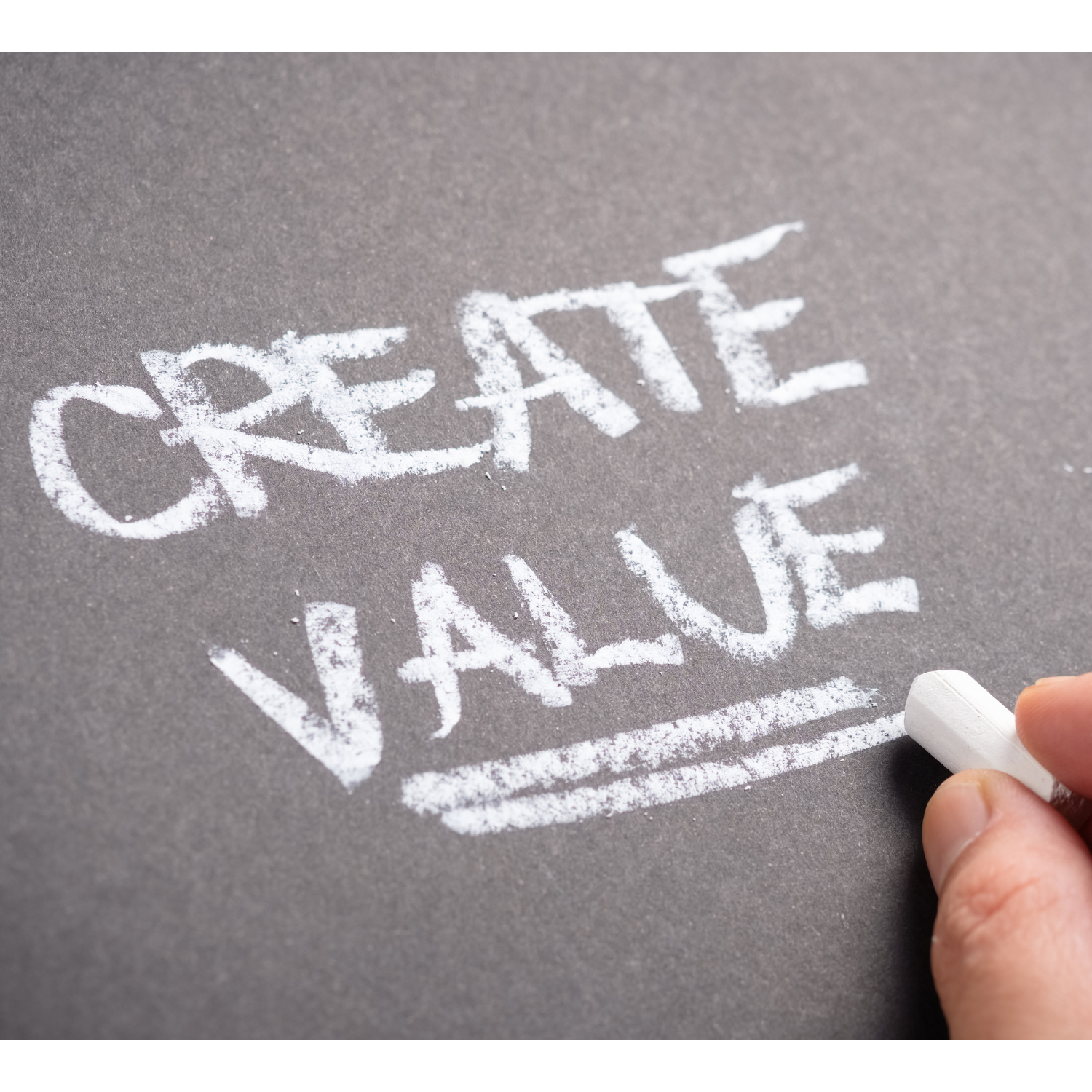 A hand writing the words "Create Value" in sidewalk chalk on a gray concrete