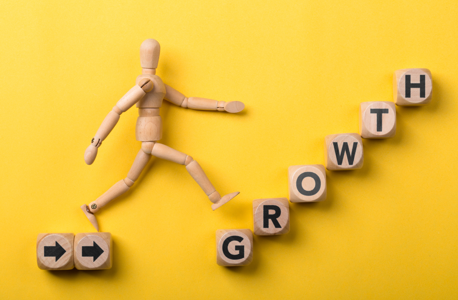 A wooden figure walking up steps that spell "Growth"