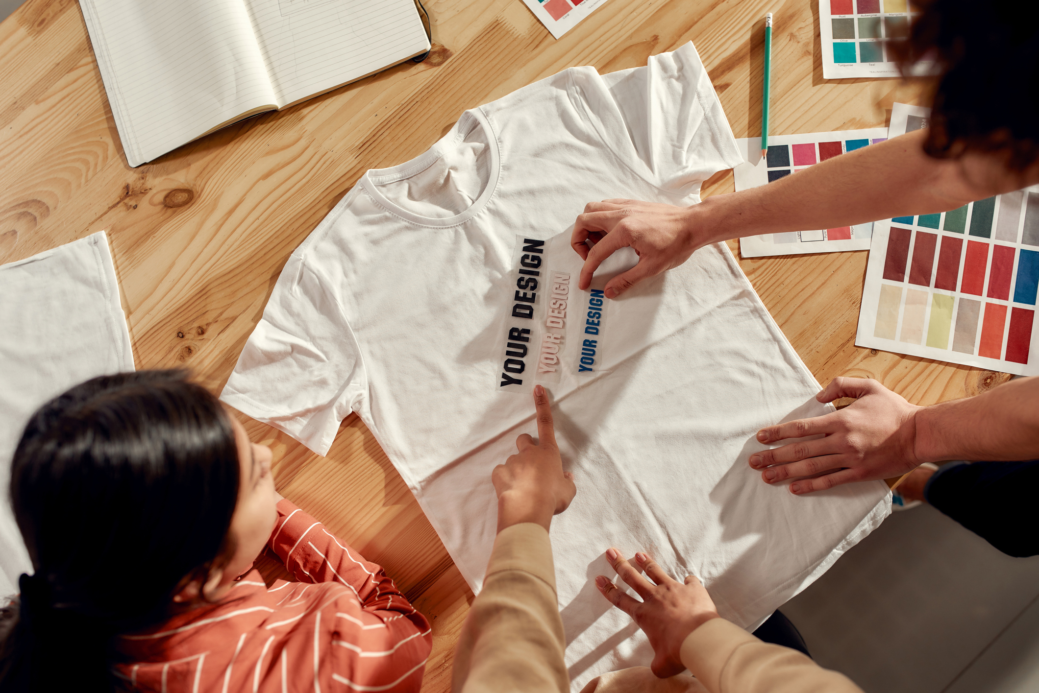 People standing over a T-shirt with "Your Design Here" text