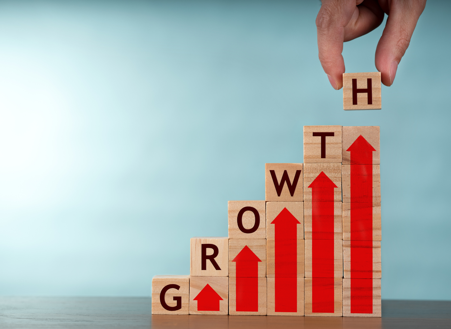 Wooden blocks creating steps spelling out the word Growth and featuring red arrows pointing up