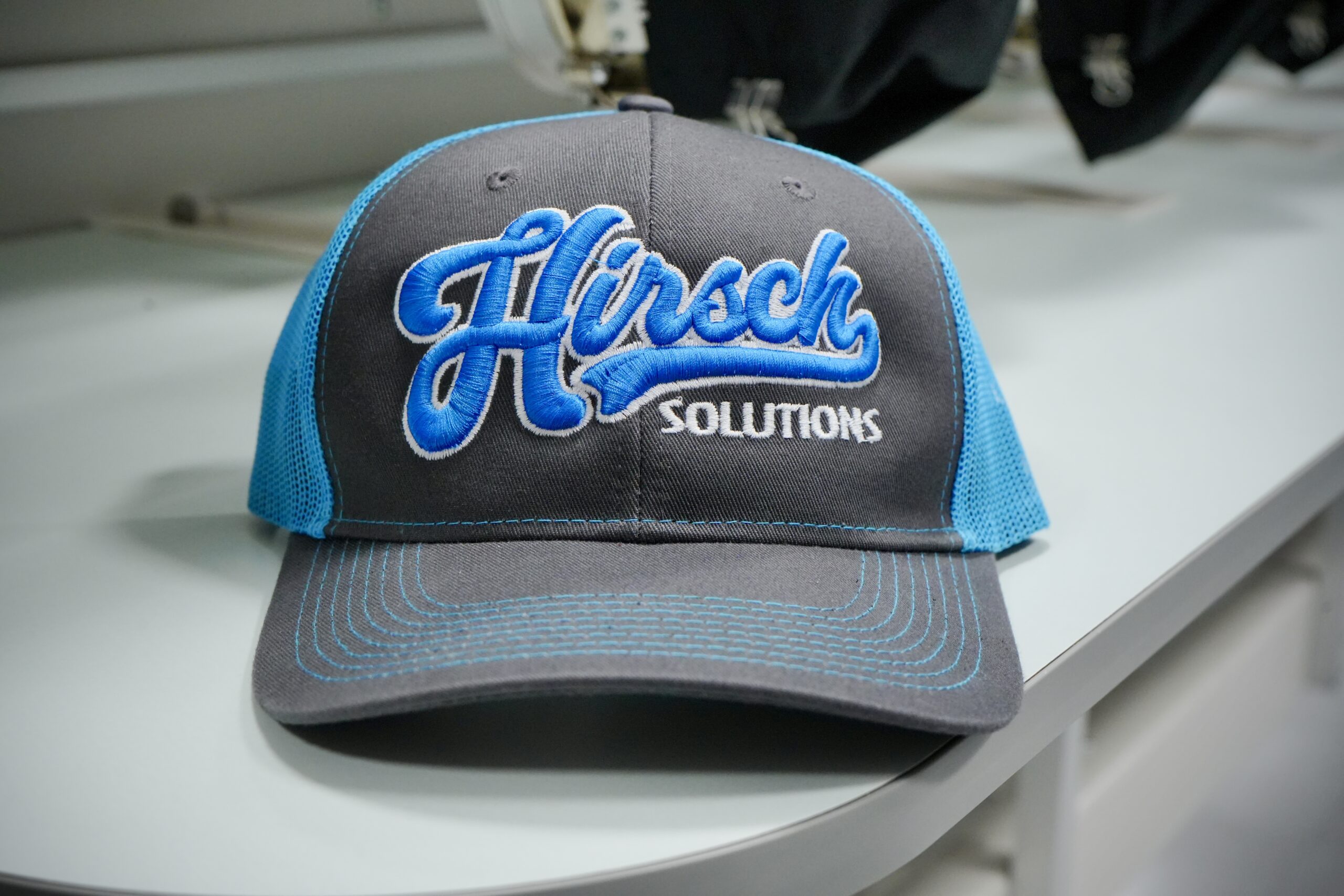 A black cap featuring Hirsch Solutions in blue puff embroidery