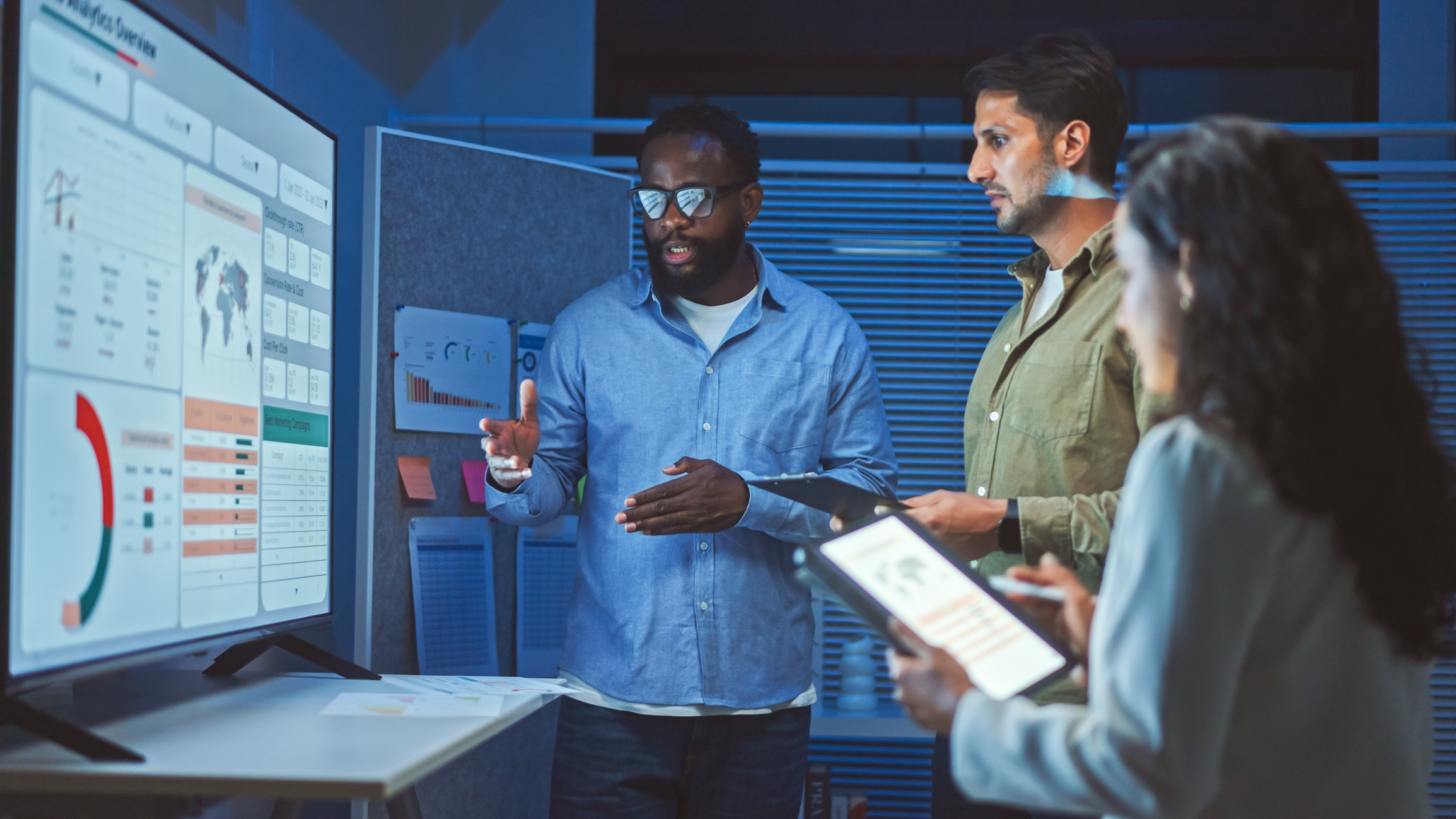 Three people standing in front of a computer screen depicting data