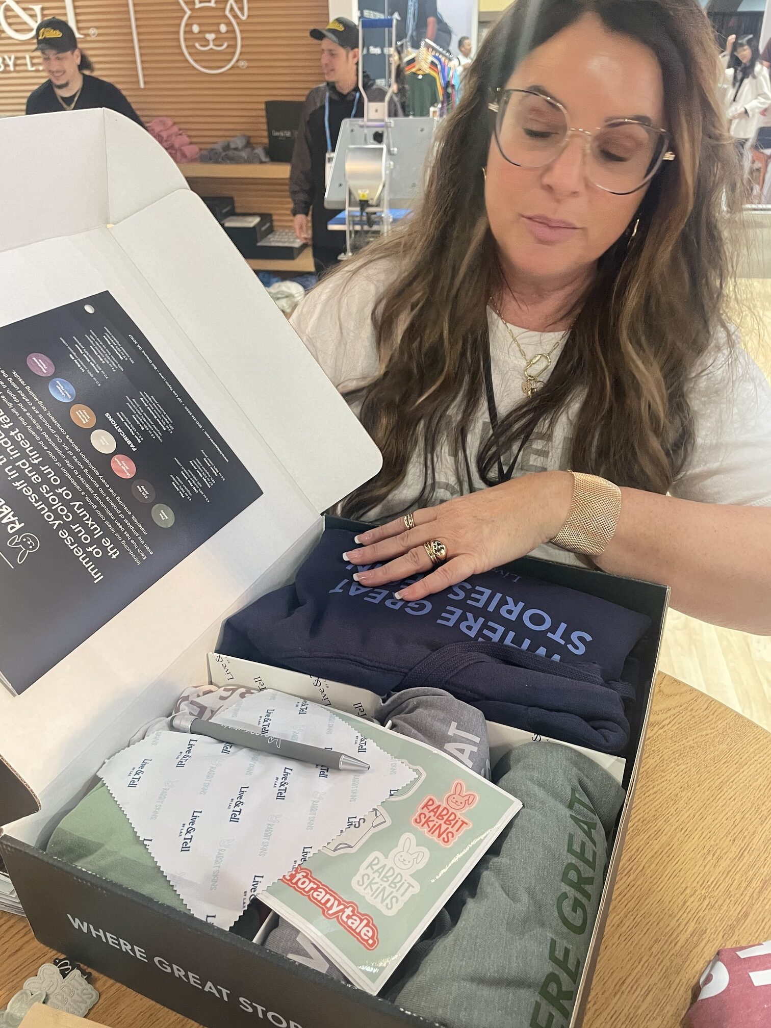 A woman points to various garments in a box printed with LAT brand logo
