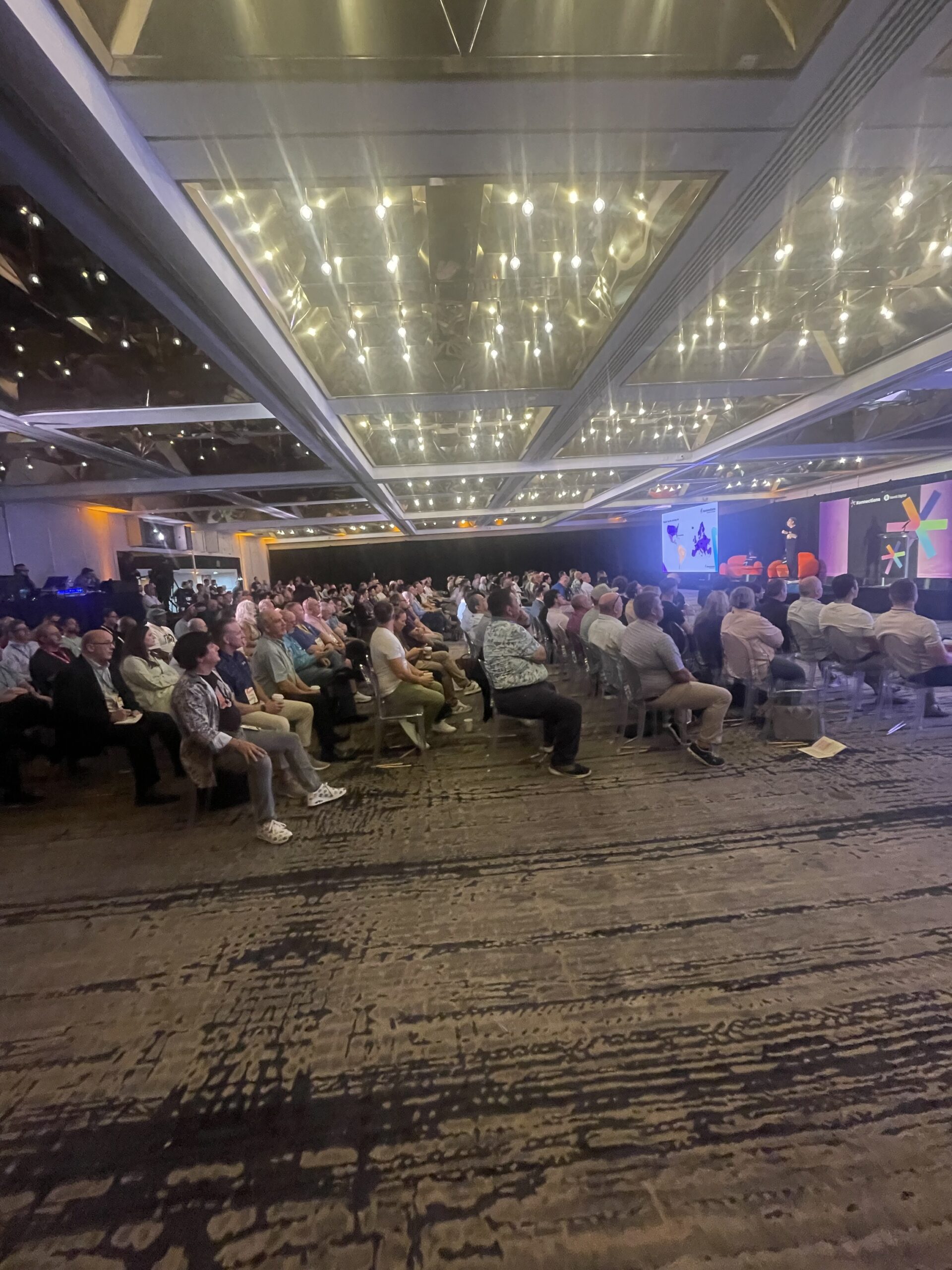 A full ballroom of attendees listening to a presentation