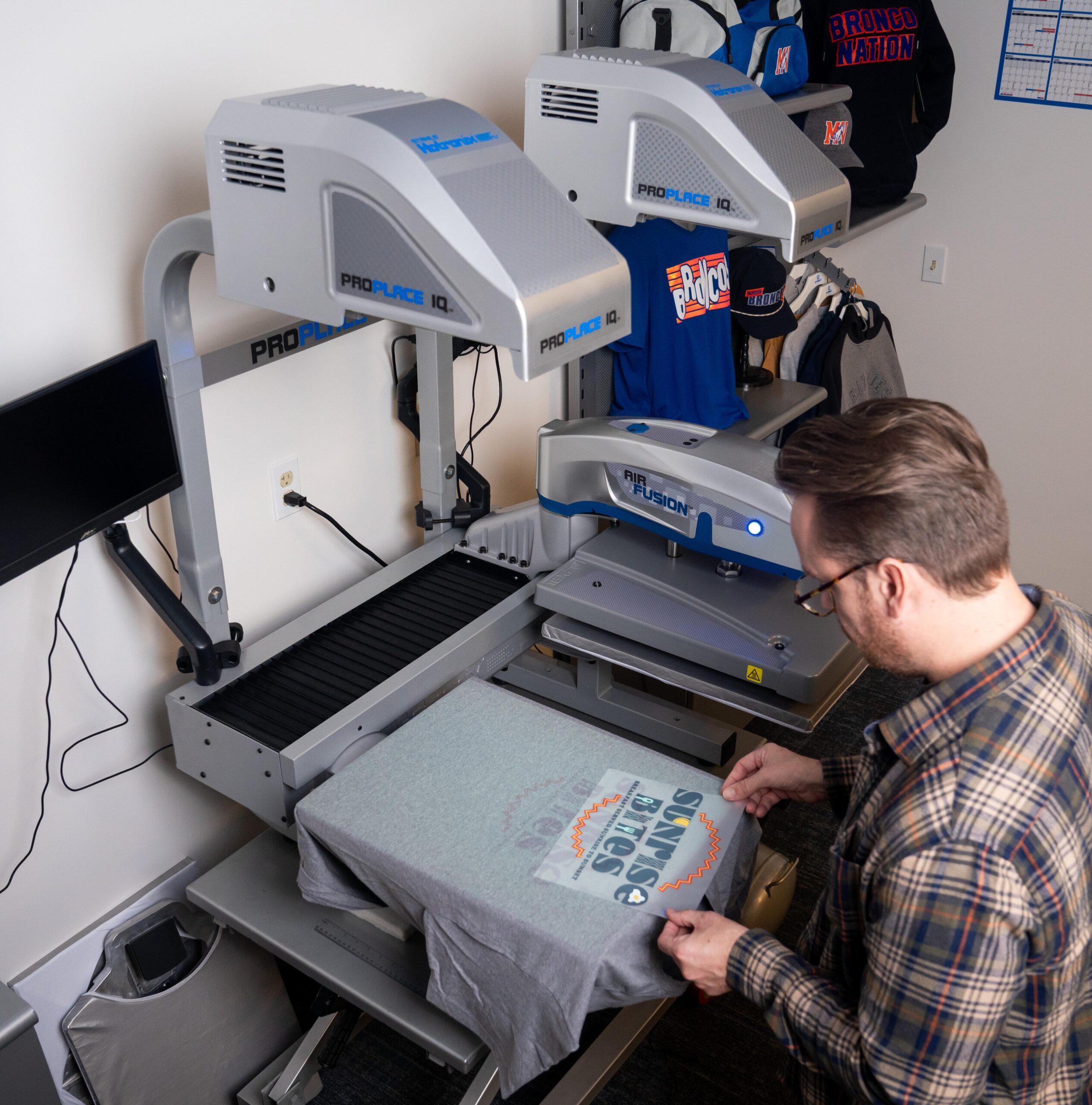 A man operating a heat press with a gray T-shirt on the platen