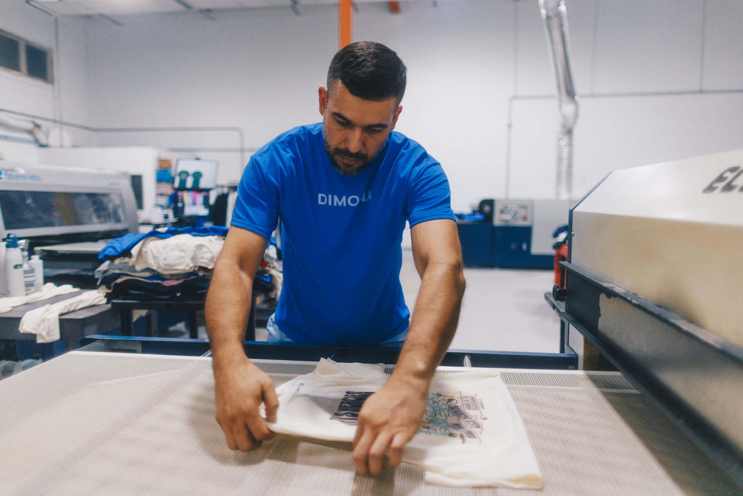 A Dimona employee wearing a blue shirt laying a white shirt on a conveyor dryer