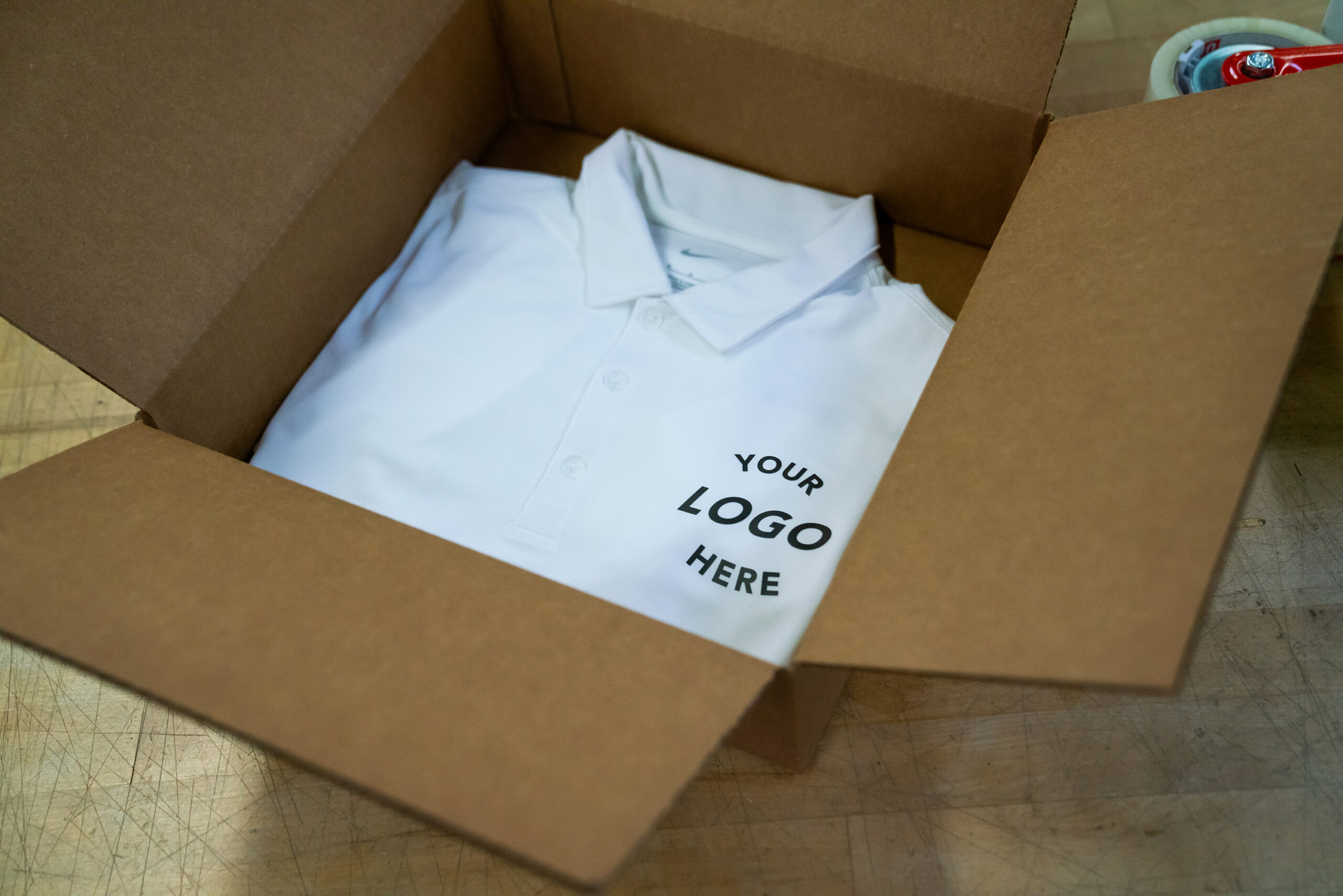 A white polo in a box with "Your Logo Here" embroidered on the left chest