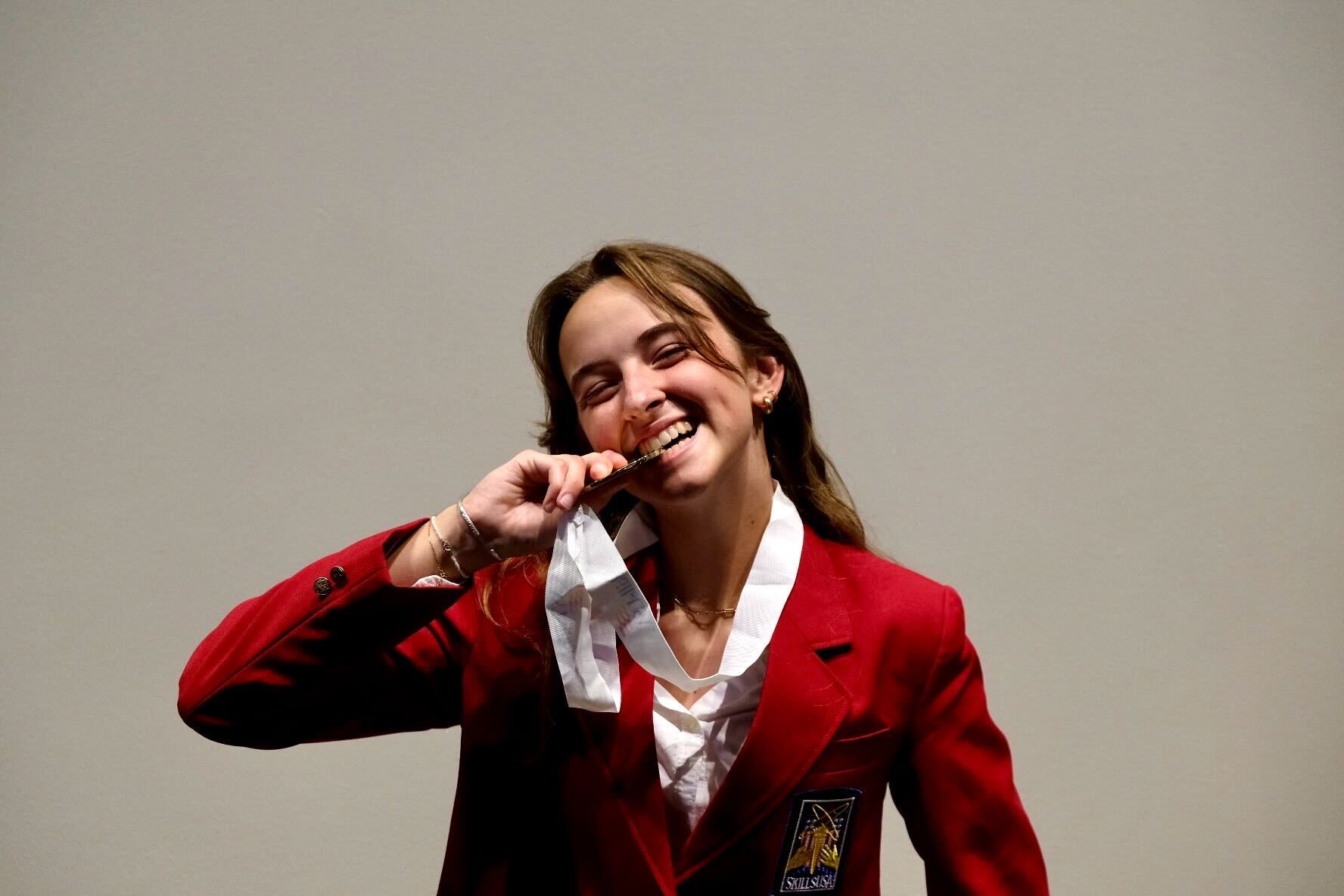 Carmen Clippinger in her red SkillsUSA jacket biting her medal