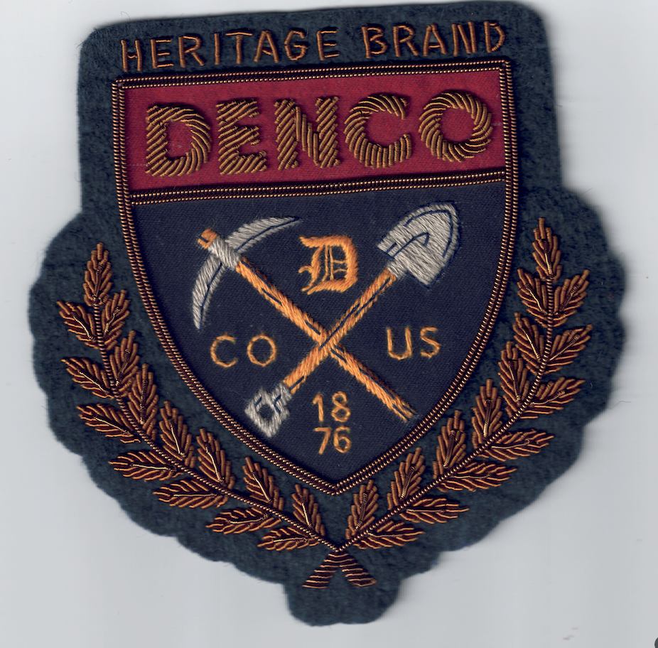 Am embroidered patch featuring the word Denco with a pick axe and shovel