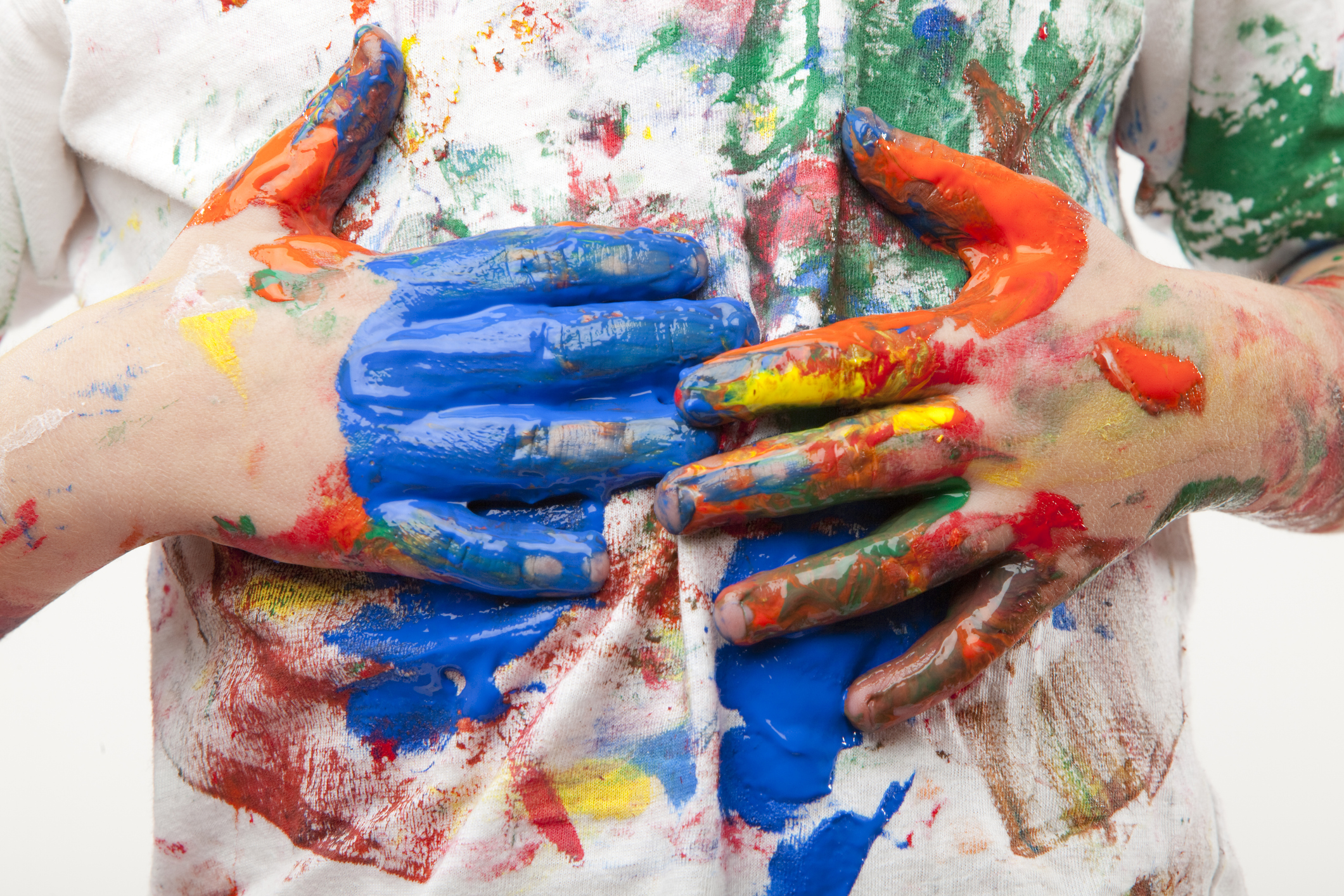 Two hands full of multi-colored paint being wiped on a white T-shirt