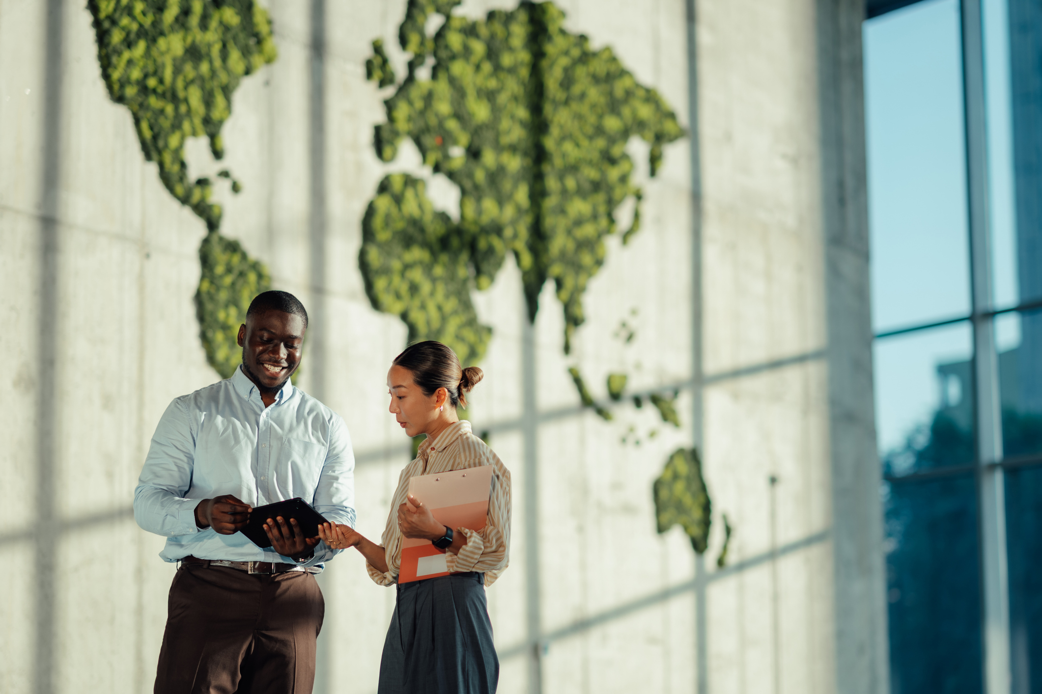 Two people looking at a file outside with a depiction of the world's countries on the wall in the background