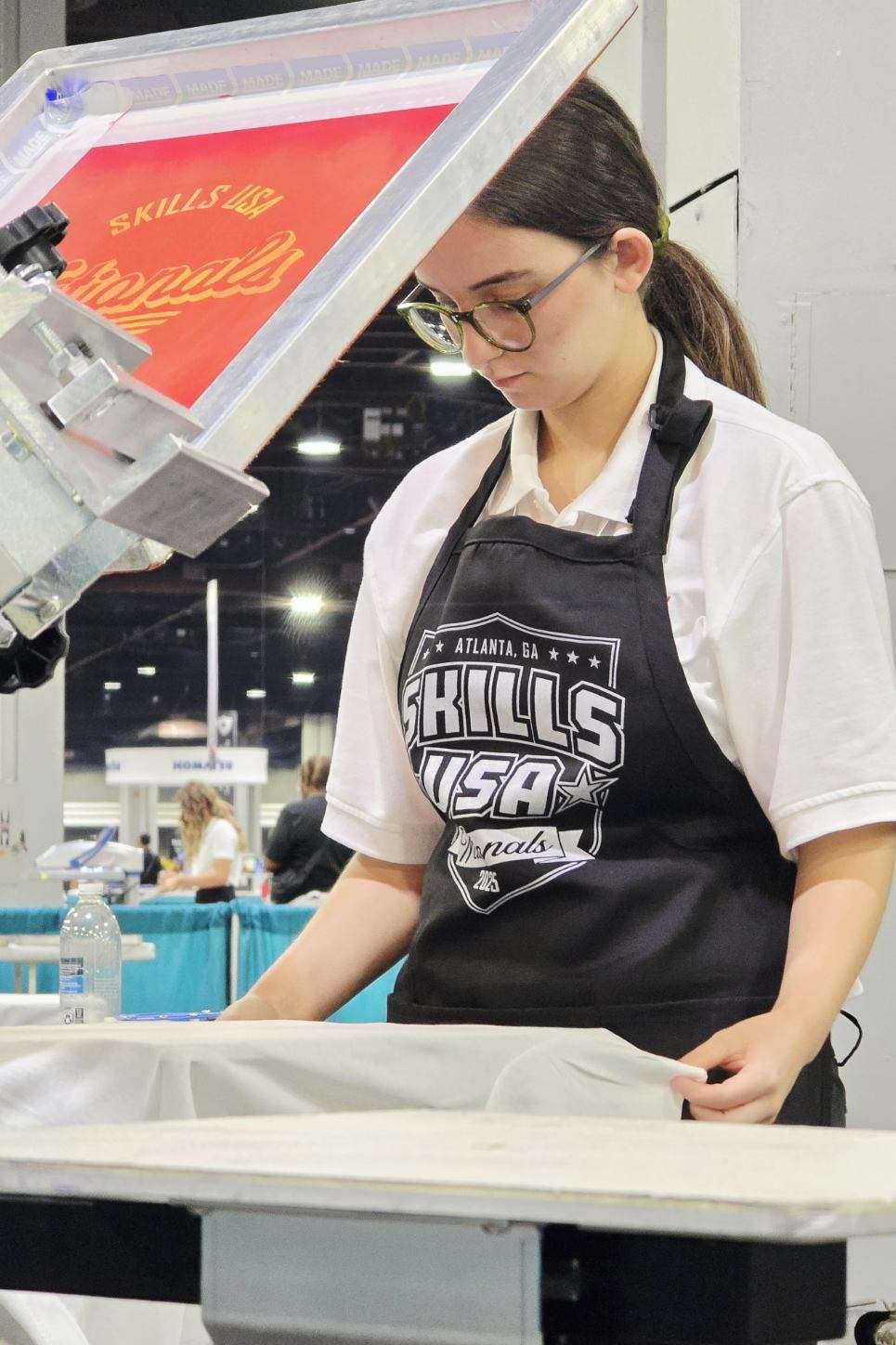 Leah Sanchez wearing her apron and adjusting a print on the screen press