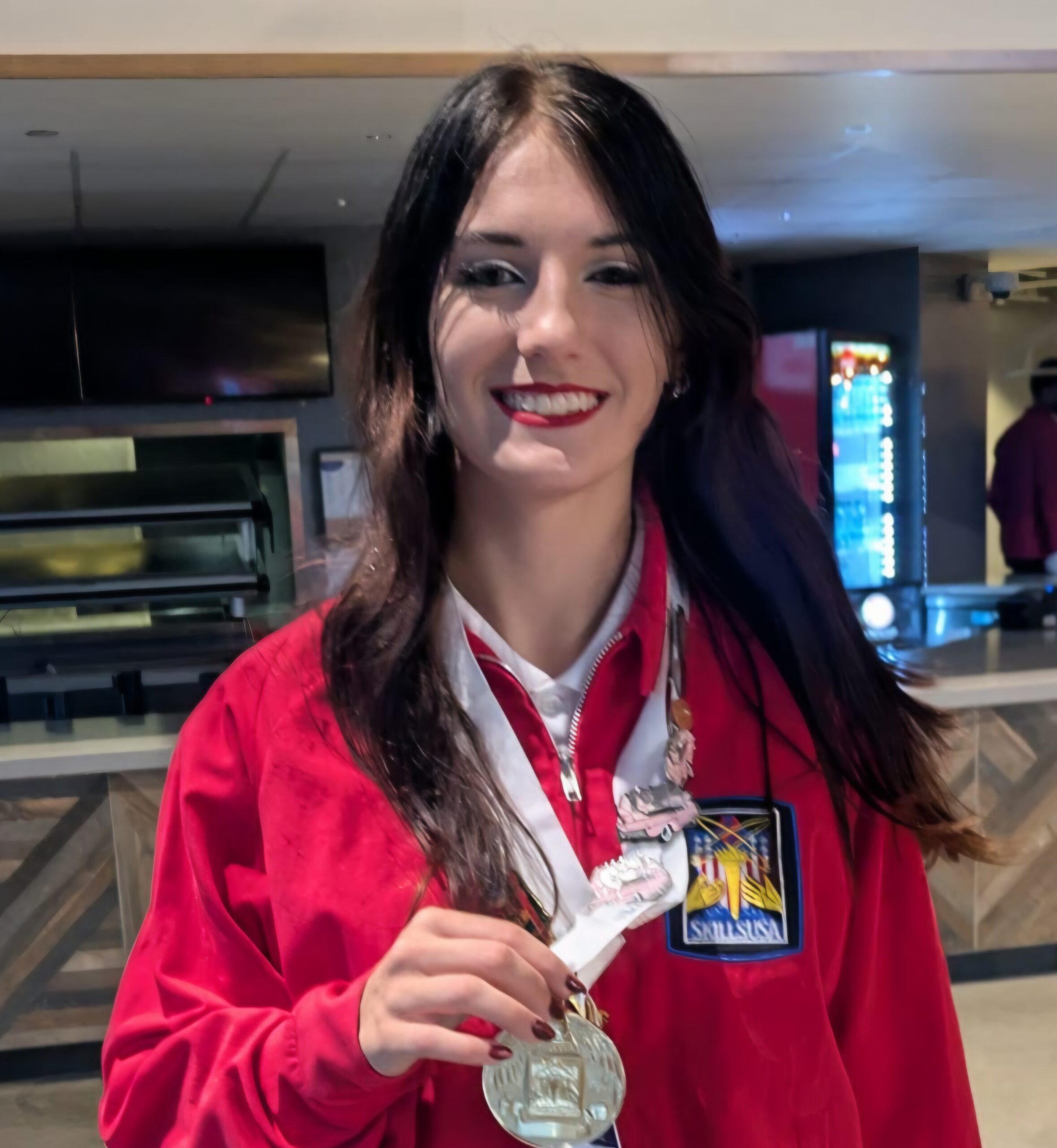 Skye Moffitt wearing her red SkillsUSA jacket and holding up her medal