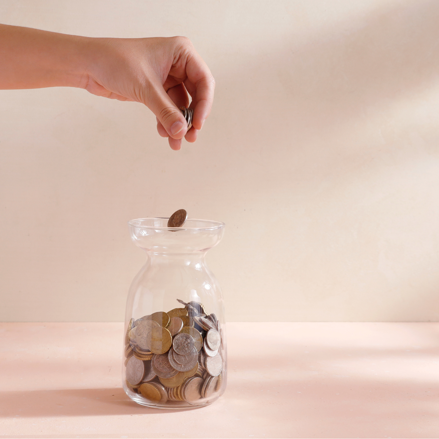 A hand dropping pennies into a glass jar