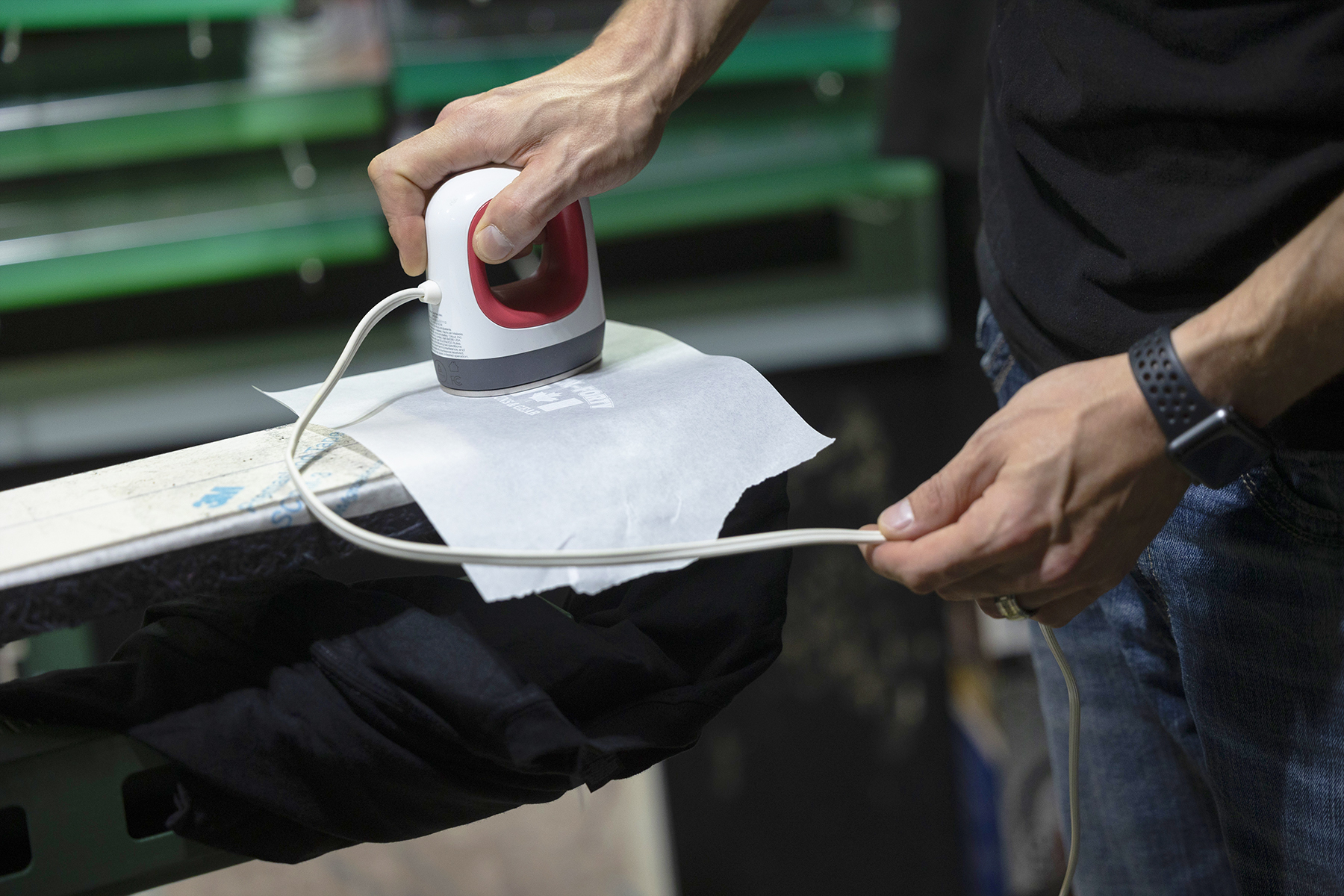 To maintain a flat, glass-like base layer of a raised print, Moulds cures the ink with a small handheld heat press while the garment is still on press.