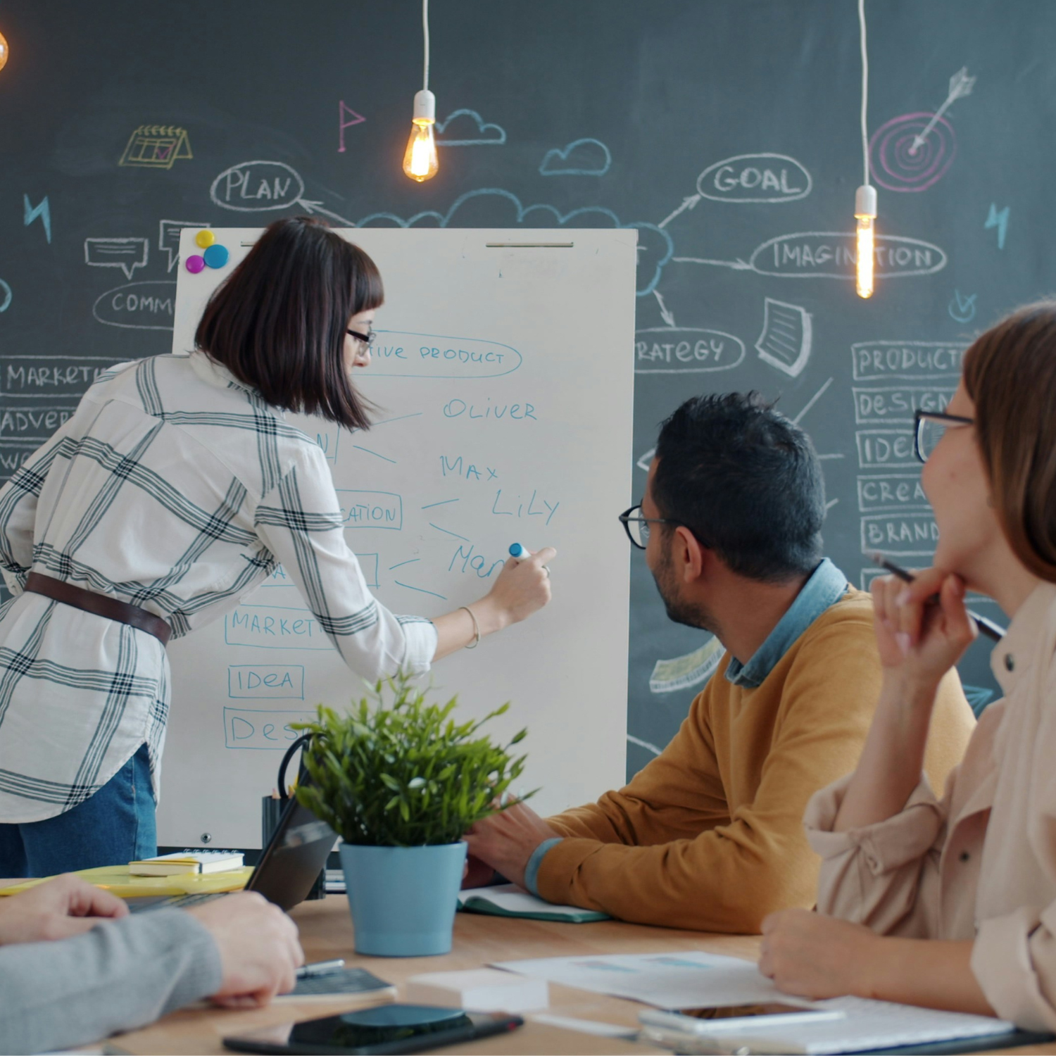 Three people having a meeting, with the one on the left writing on a white board
