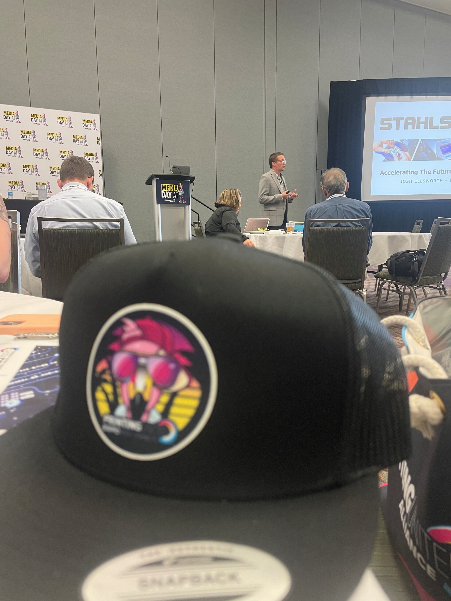 A perspective of a speaker in the background with a blurred out hat in the foreground