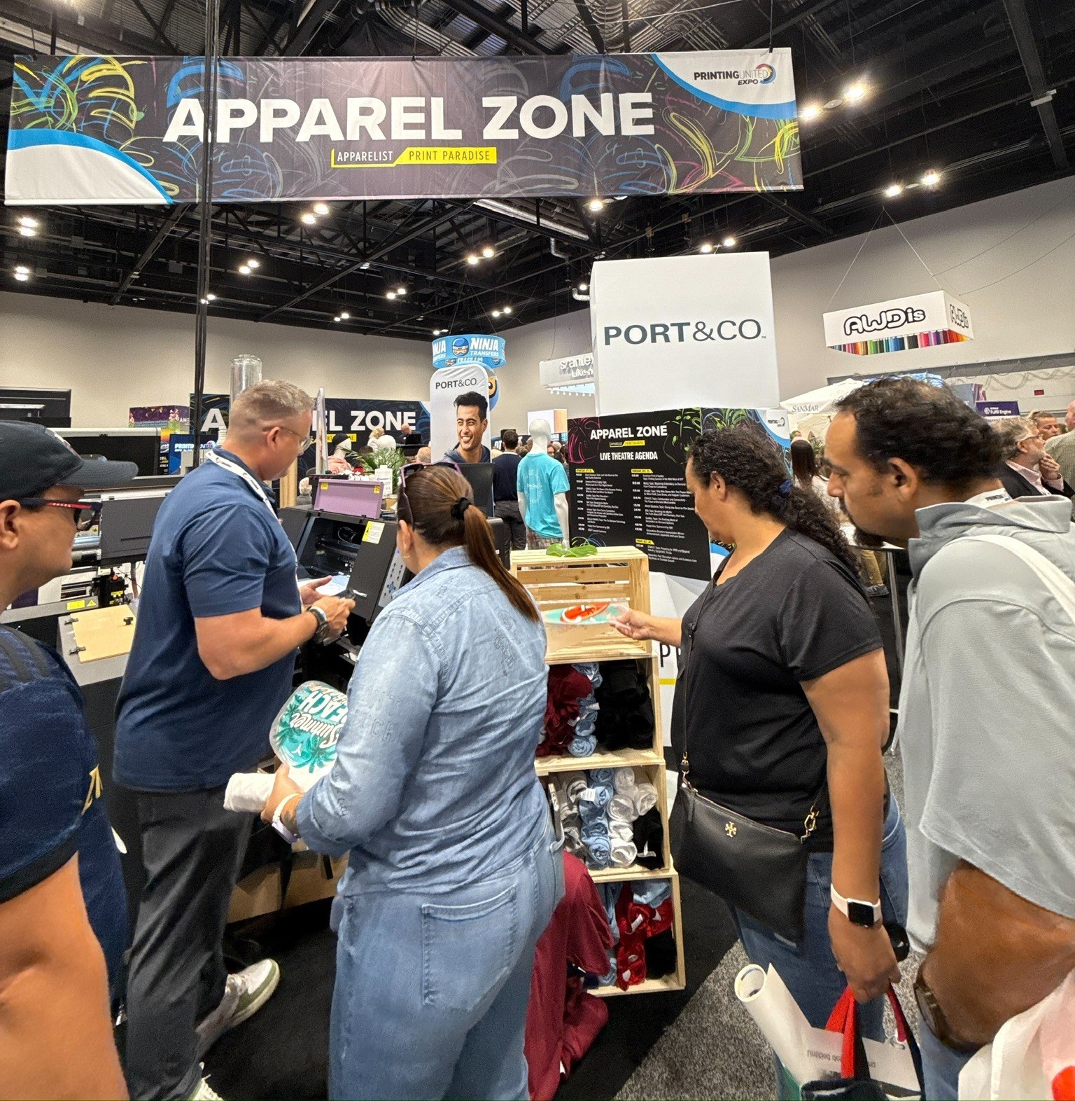 People gathered around a printer with Apparel Zone banner in the background