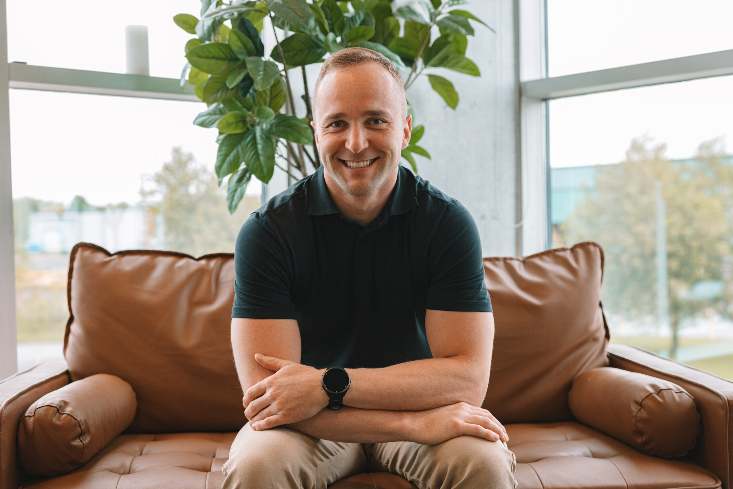 Alex Sckoropad wearing black shirt sitting on brown couch