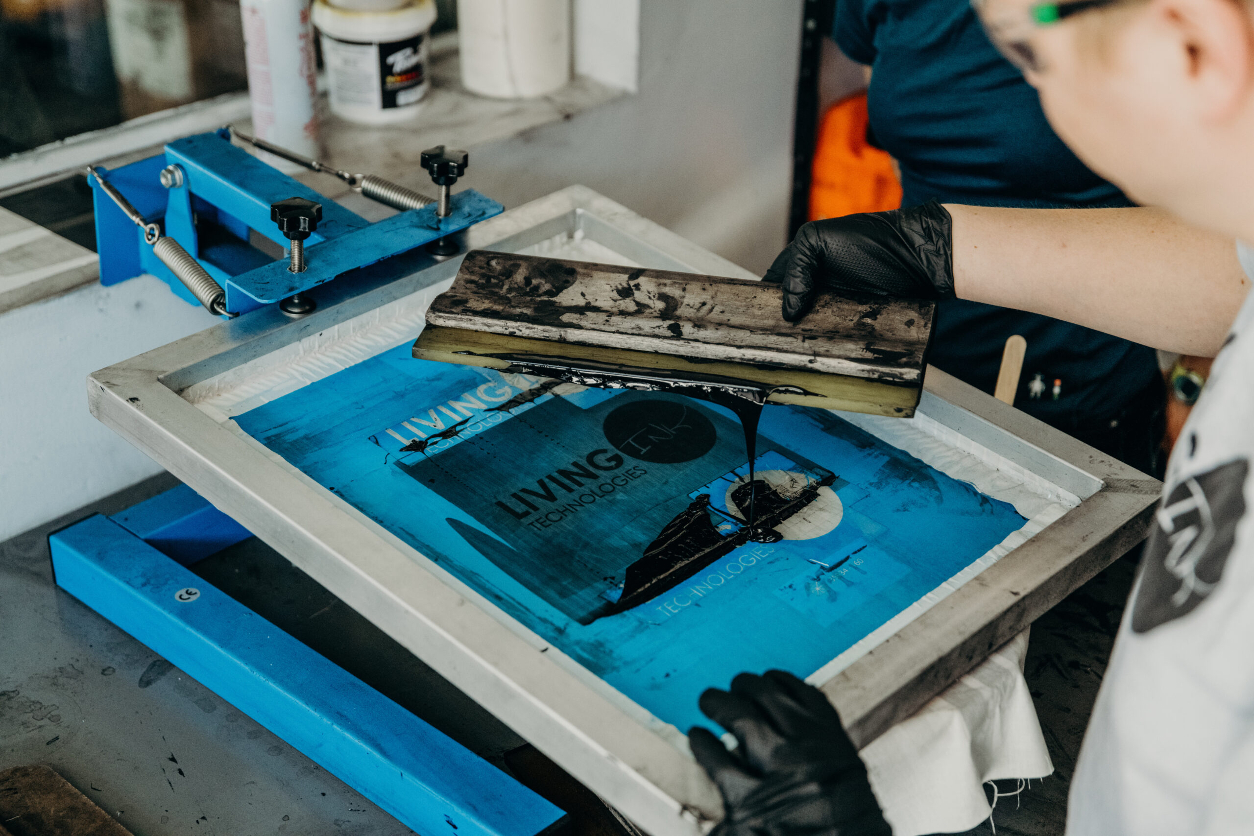 A person pulling a squeegee across a screen with black ink